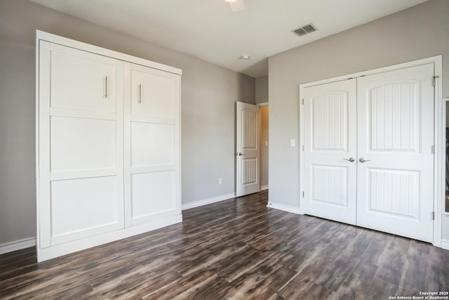 unfurnished bedroom with dark wood-style flooring, a closet, visible vents, and baseboards