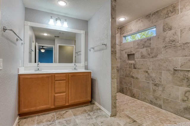 full bathroom with double vanity, a walk in shower, a textured wall, and a sink