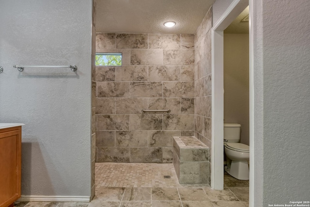 bathroom with a tile shower, a textured ceiling, toilet, and a textured wall