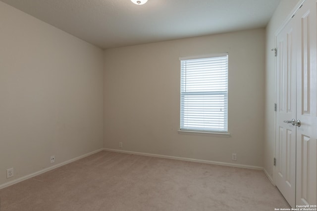 spare room featuring baseboards and light carpet