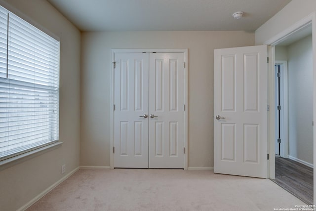 unfurnished bedroom with light colored carpet, a closet, and baseboards