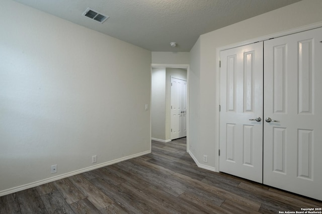 unfurnished bedroom with dark wood-style floors, visible vents, baseboards, a closet, and a textured ceiling