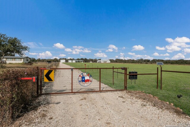 view of gate featuring a rural view, a lawn, and fence