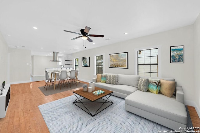 living area with light wood-type flooring, ceiling fan, a wealth of natural light, and recessed lighting