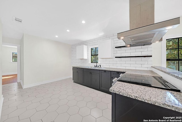 kitchen featuring visible vents, island range hood, baseboards, light stone countertops, and backsplash