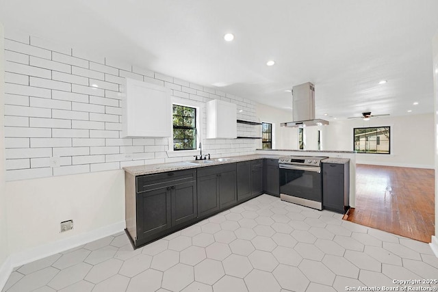 kitchen featuring island exhaust hood, a sink, light stone countertops, a peninsula, and stainless steel electric range