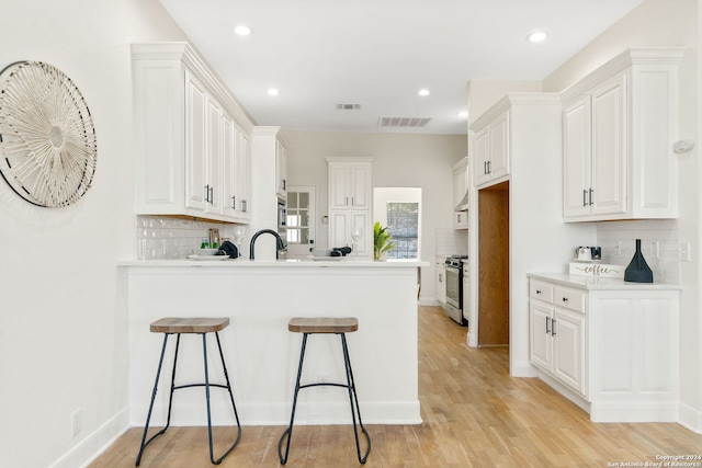 11217 Cave Crk, Helotes, TX 78023 - kitchen with stainless steel gas range oven, a peninsula, a breakfast bar, white cabinetry, and light wood-style floors