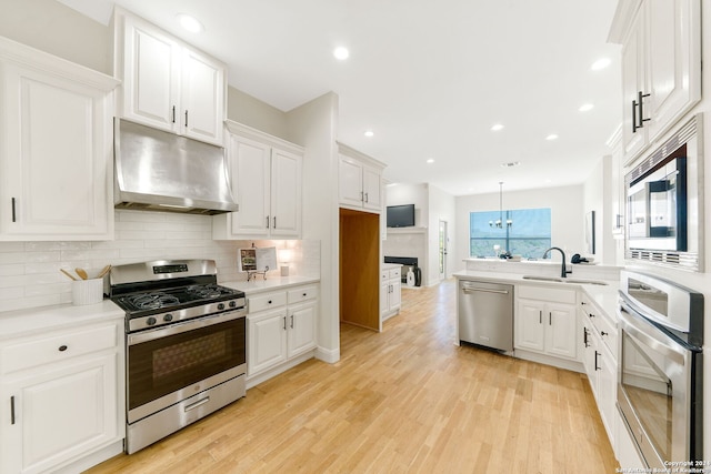 11217 Cave Crk, Helotes, TX 78023 - kitchen with under cabinet range hood, stainless steel appliances, white cabinetry, light wood-type flooring, and backsplash