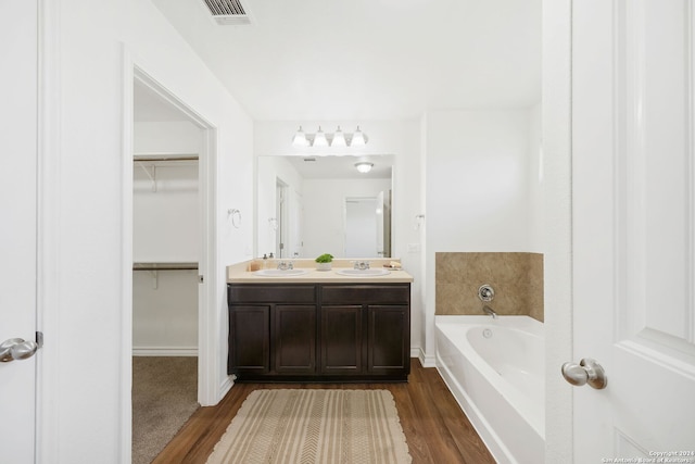 bathroom with visible vents, wood finished floors, a sink, a walk in closet, and a bath