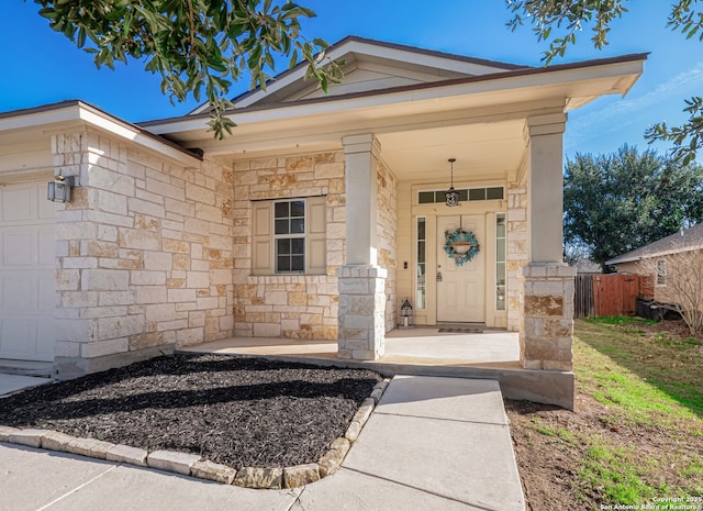 doorway to property featuring stone siding, a porch, an attached garage, and fence