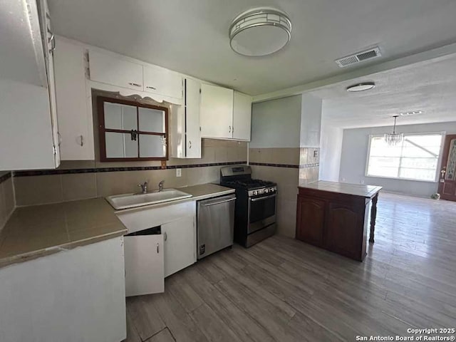 kitchen with visible vents, a peninsula, stainless steel appliances, white cabinetry, and a sink