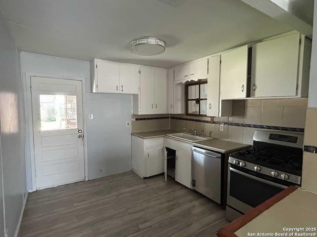 kitchen with white cabinets, appliances with stainless steel finishes, wood finished floors, a sink, and backsplash