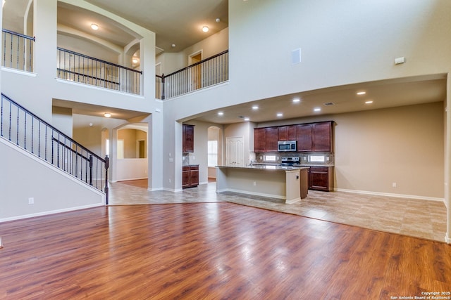 unfurnished living room with baseboards, arched walkways, light wood-style flooring, stairway, and recessed lighting