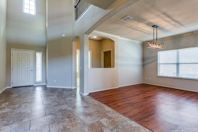 foyer entrance featuring arched walkways, crown molding, visible vents, and baseboards