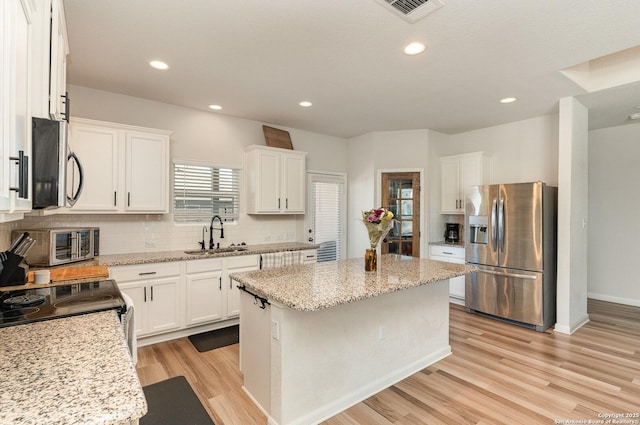 kitchen with stainless steel appliances, a sink, visible vents, a center island, and decorative backsplash