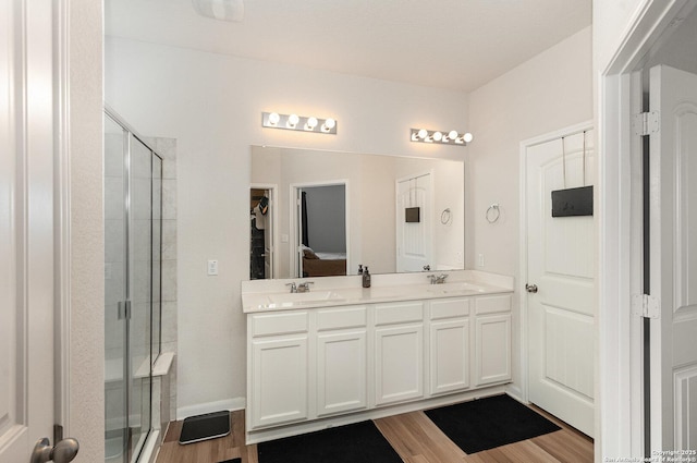 bathroom with double vanity, a stall shower, a sink, and wood finished floors