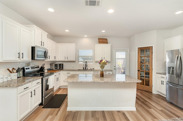 kitchen with a sink, visible vents, light wood-style floors, appliances with stainless steel finishes, and a center island