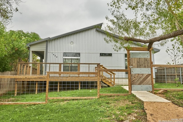 rear view of house featuring fence, a wooden deck, and a lawn