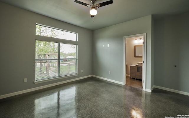 unfurnished bedroom featuring dark speckled floor, connected bathroom, a ceiling fan, and baseboards