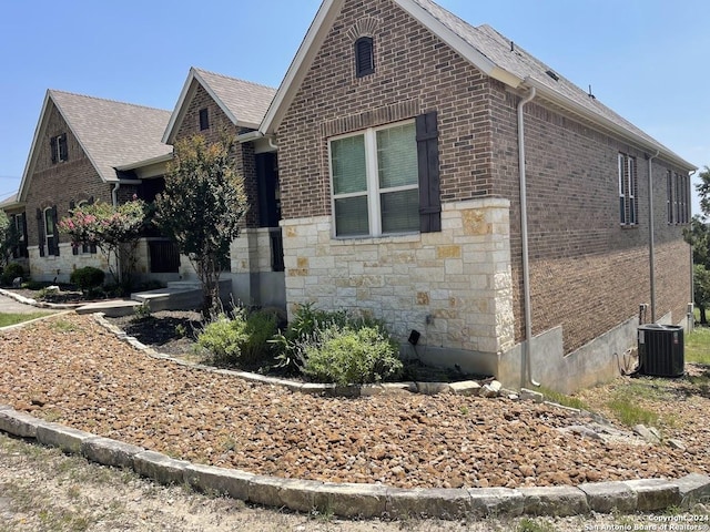 view of property exterior featuring stone siding, brick siding, and central AC unit
