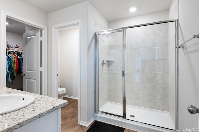 full bathroom with a spacious closet, toilet, vanity, a shower stall, and wood finished floors