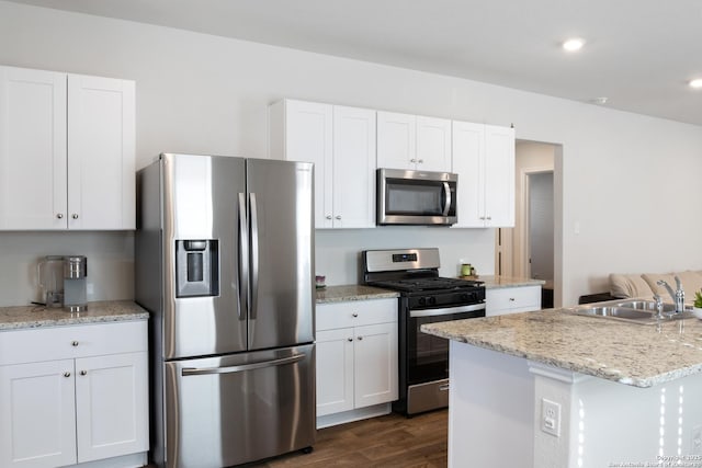 kitchen featuring stainless steel appliances, a sink, white cabinets, light stone countertops, and dark wood finished floors