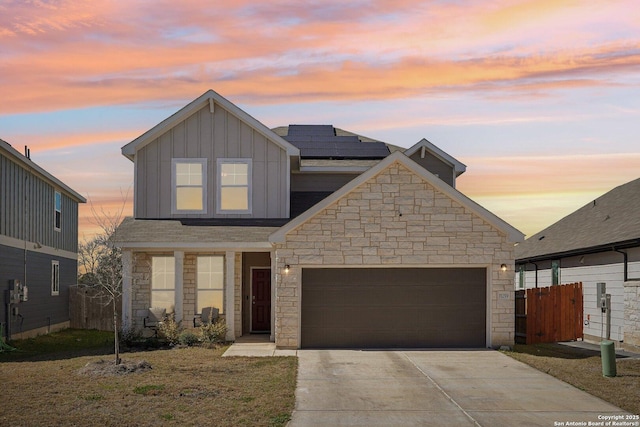 traditional-style house with an attached garage, fence, concrete driveway, stone siding, and board and batten siding