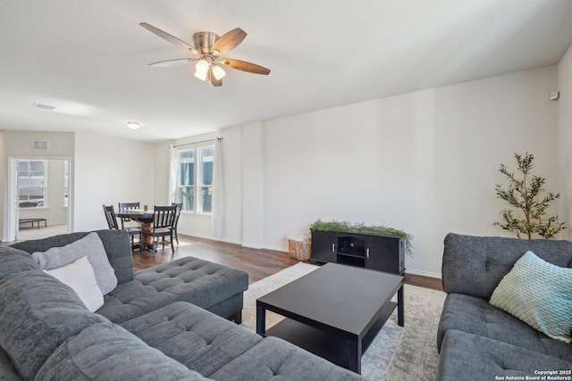 living area with visible vents, ceiling fan, baseboards, and wood finished floors