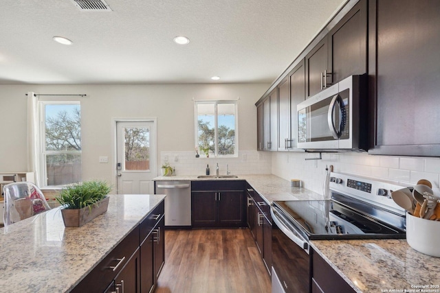 kitchen with dark brown cabinetry, tasteful backsplash, appliances with stainless steel finishes, light stone counters, and dark wood-type flooring