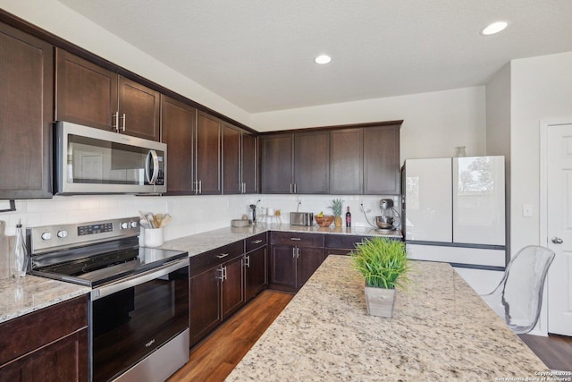 kitchen with stainless steel appliances, light stone counters, dark brown cabinetry, and decorative backsplash