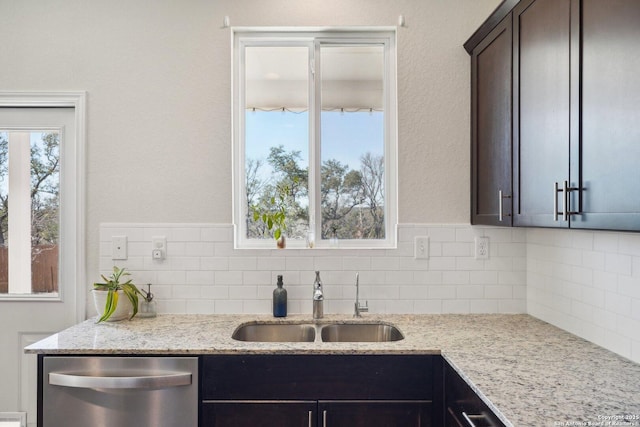 kitchen featuring stainless steel dishwasher, light stone counters, backsplash, and a sink