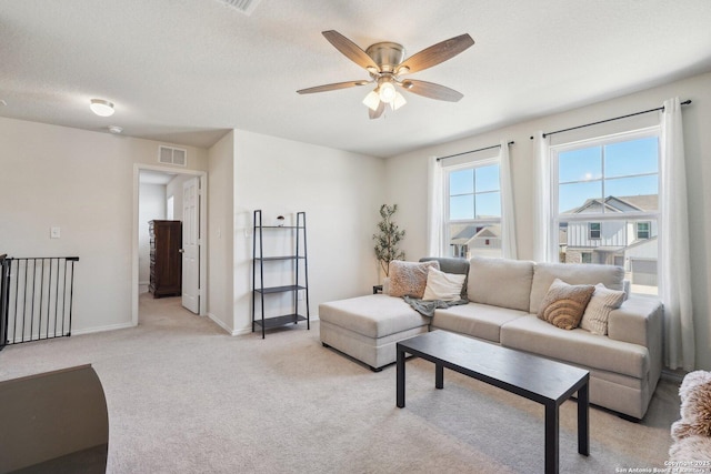 living area featuring light colored carpet, visible vents, a ceiling fan, a textured ceiling, and baseboards