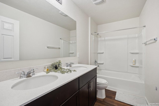 bathroom featuring toilet, double vanity, a sink, and wood finished floors