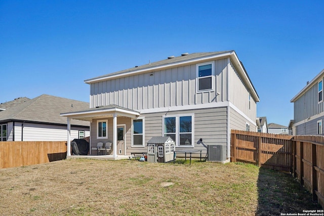 rear view of house featuring a patio, a lawn, central AC unit, board and batten siding, and a fenced backyard