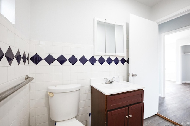 half bathroom with toilet, wood finished floors, vanity, and tile walls