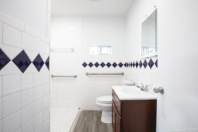 full bath with toilet, wood finished floors, a tile shower, vanity, and tile walls