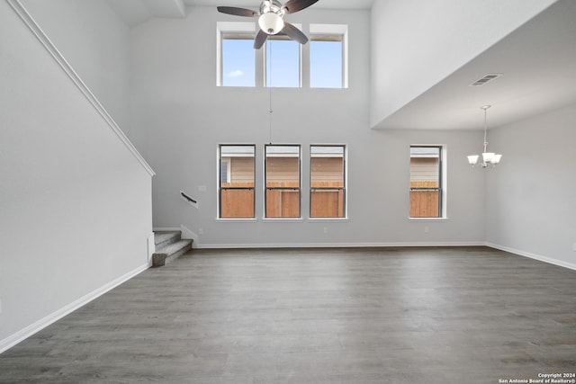 unfurnished living room with dark wood finished floors, stairway, baseboards, and ceiling fan with notable chandelier