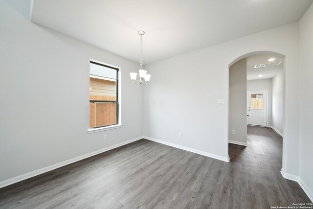 empty room featuring baseboards, visible vents, arched walkways, dark wood-type flooring, and a wealth of natural light