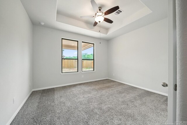 spare room with carpet, a raised ceiling, visible vents, and baseboards