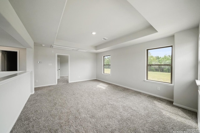 carpeted empty room featuring a raised ceiling and baseboards