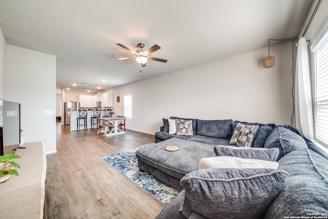 living area featuring a ceiling fan, a wealth of natural light, baseboards, and wood finished floors