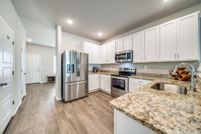 kitchen featuring appliances with stainless steel finishes, a sink, light wood finished floors, and light stone counters