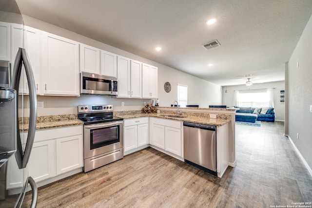 kitchen featuring a peninsula, visible vents, white cabinetry, open floor plan, and appliances with stainless steel finishes