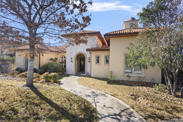 mediterranean / spanish-style home featuring stone siding, a tile roof, a chimney, and stucco siding