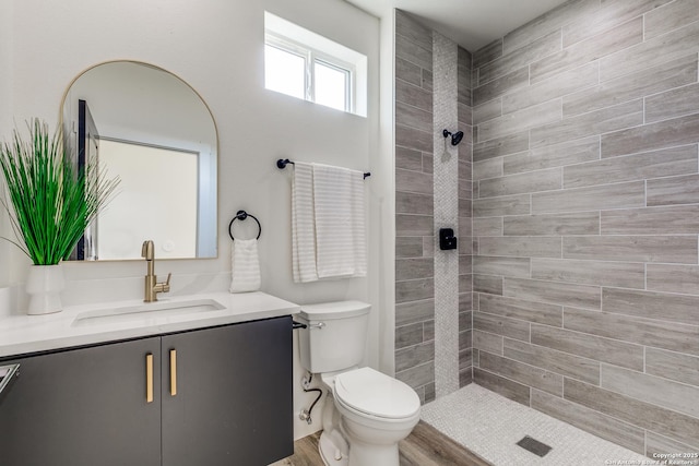 full bathroom featuring a tile shower, vanity, and toilet