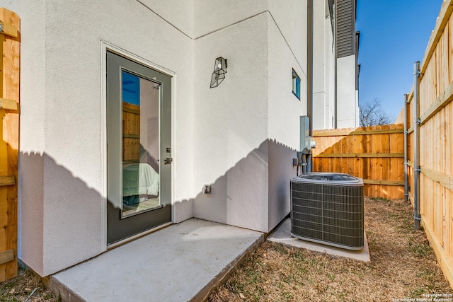 entrance to property with fence, central AC unit, and stucco siding