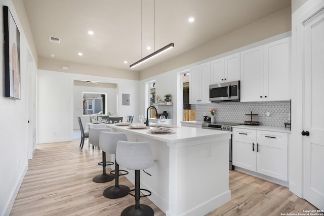 kitchen featuring appliances with stainless steel finishes, light wood-type flooring, decorative backsplash, and an island with sink