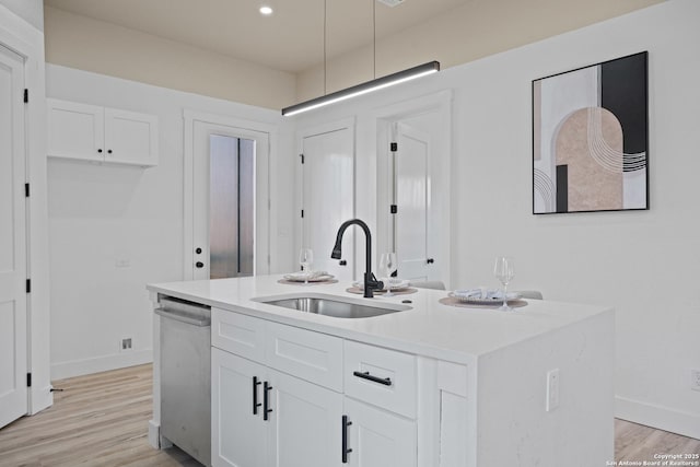 kitchen with a kitchen island with sink, light countertops, stainless steel dishwasher, white cabinetry, and a sink