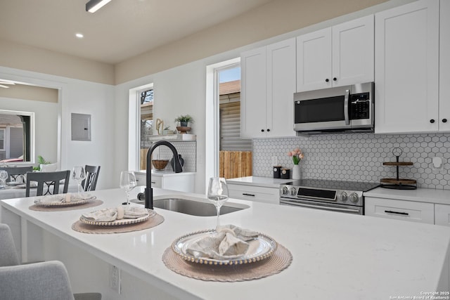 kitchen featuring decorative backsplash, stainless steel appliances, a kitchen bar, white cabinetry, and a sink