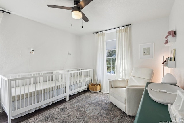 bedroom with a crib, ceiling fan, and wood finished floors